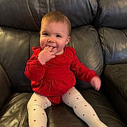 Aspen joined the competition — help win amazing prizes! baby, child, red_clothing, white_tights, sitting, leather_couch, indoor, happy, smiling, cute, portrait, infant, fingers_in_mouth, casual, home, young_child, toddler, cozy, comfortable, playful