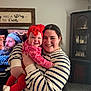 Aspen is registered to the contest to win money with this photo: baby, cabinet, child, clothing, cozy, cute, family, furniture, happy, holding, home_interior, indoor, living_room, person, portrait, red_headband, smile, striped_sweater, television, woman