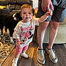 toddler, child, minnie_mouse, shirt, shorts, sneakers, hand_holding, adult, dog, living_room, carpet, couch, wood_floor, person, smile, indoor, furniture, family, pet, home