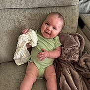 Aspen is registered to the contest to win money with this photo: baby, infant, smiling, green_onesie, couch, blanket, white_cloth, happy, sitting, indoors, soft_texture, cute, child, person, comfortable, cozy, relaxed, portrait, skin, face