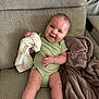 baby, infant, smiling, green_onesie, couch, blanket, white_cloth, happy, sitting, indoors, soft_texture, cute, child, person, comfortable, cozy, relaxed, portrait, skin, face