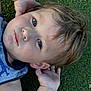 toddler, child, face, blue_eyes, grass, outdoor, hands, hair, tank_top, dinosaur, casual_clothing, skin, portrait, young_child, expression, laying_down, nature, daylight, close_up, cute