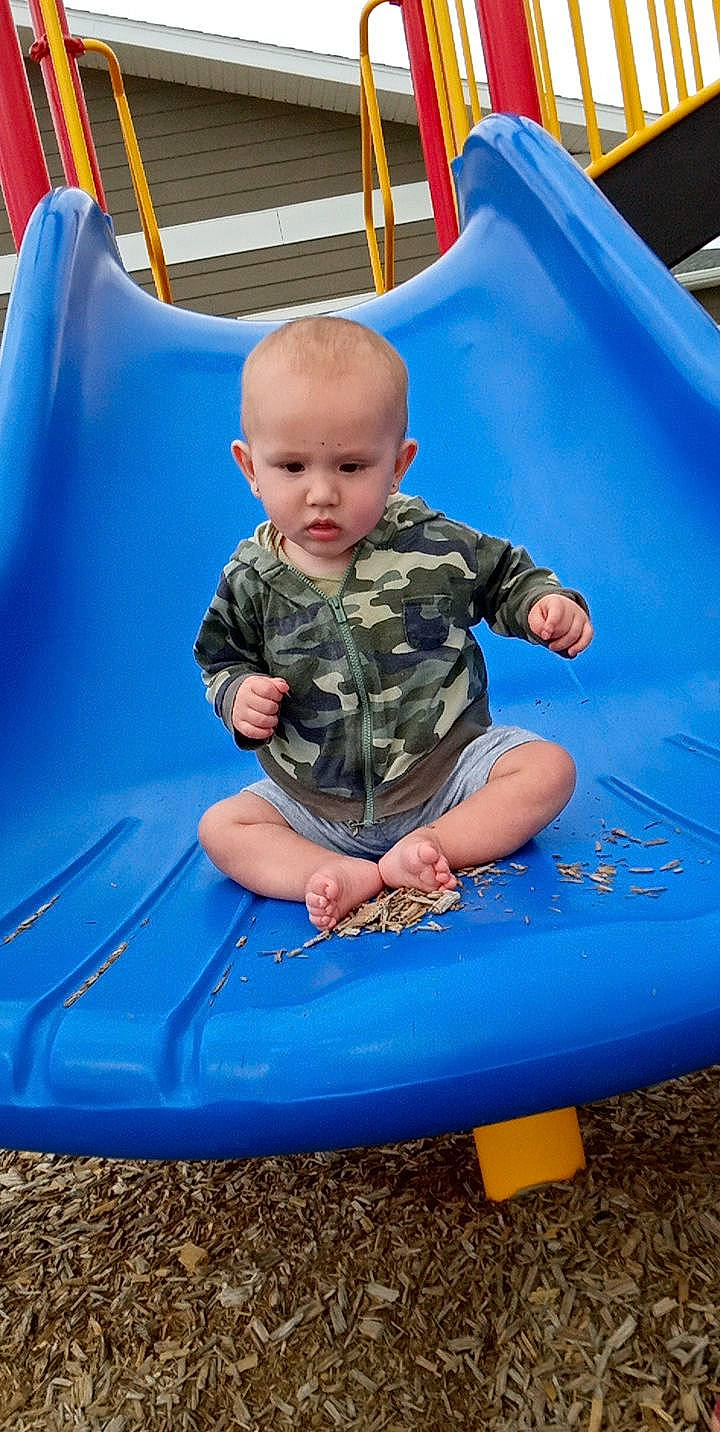 William is registered to the contest to win money with this photo: baby_toddler_clothing, blue, child, comfort, electric_blue, fun, games, grass, leisure, outdoor_play_equipment, outdoor_recreation, person, photograph, playground, recreation, shorts, sitting, summer, t_shirt, toddler