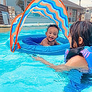 Liam is registered to the contest to win money with this photo: baby, child, pool, swimming_pool, water, float, inflatable, canopy, life_jacket, smile, happy, outdoor, summer, fun, play, water_play, person, backyard, house, recreation