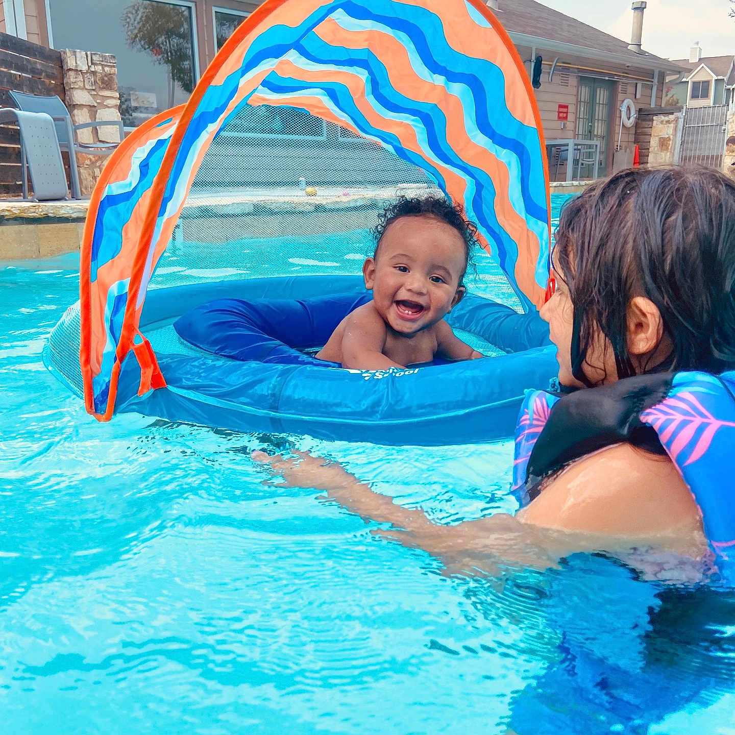 Liam is registered to the contest to win money with this photo: baby, child, pool, swimming_pool, water, float, inflatable, canopy, life_jacket, smile, happy, outdoor, summer, fun, play, water_play, person, backyard, house, recreation