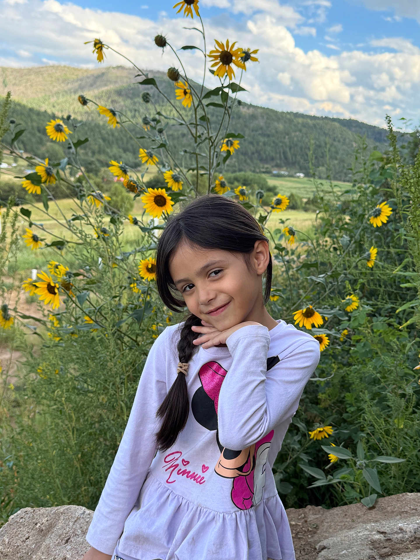 Heavenly Faith is registered to the contest to win money with this photo: braid, casual_clothing, child, clouds, daylight, field, flowers, girl, greenery, hill, long_sleeve, nature, outdoor, plants, playful, portrait, sky, smile, sunflowers, young