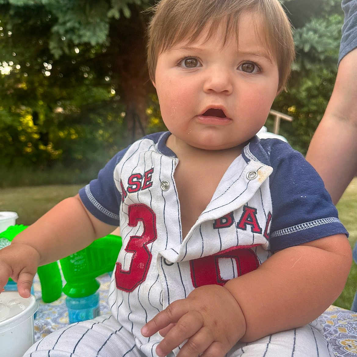 Callum joined the competition — help win amazing prizes! toddler, child, baby, outdoor, greenery, baseball_outfit, striped_clothing, curious_expression, sitting, summer, daylight, portrait, young_child, cute, plump_arms, short_hair, table, hand, person, nature