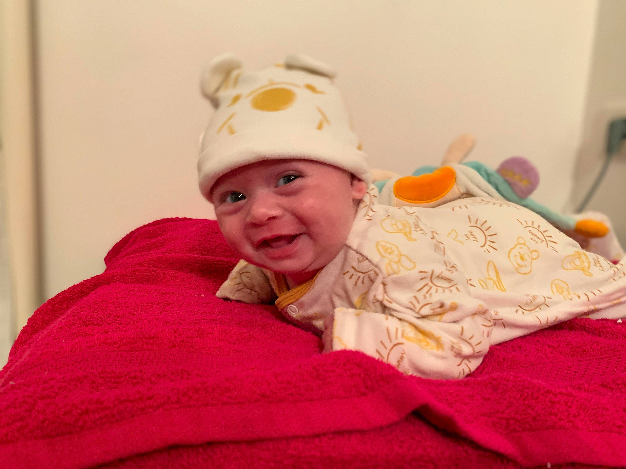 Mily participe au concours pour gagner de l'argent avec cette photo : baby, baby_products, baby_toddler_clothing, beanie, cap, cheek, child, comfort, fashion_accessory, happy, headwear, laugh, linens, magenta, outerwear, peach, person, room, sitting, sleeve