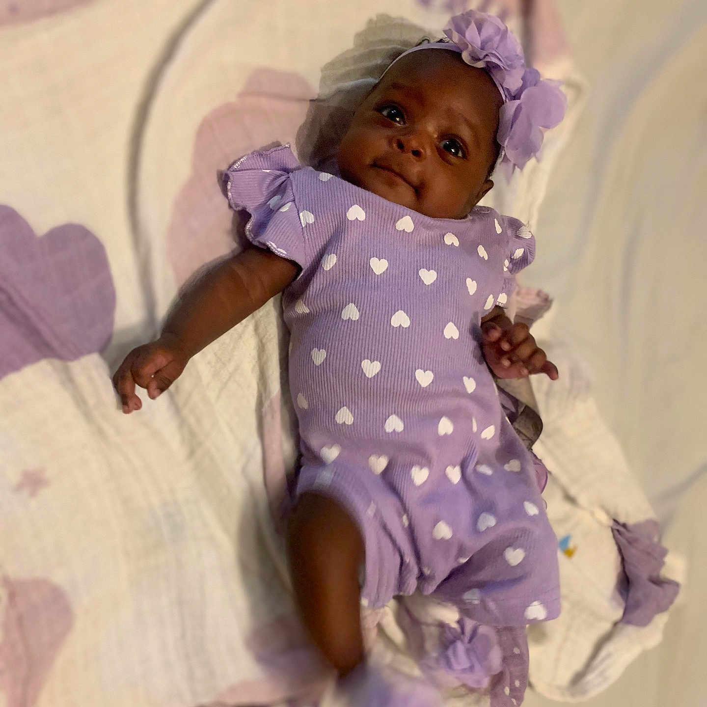 Journei is registered to the contest to win money with this photo: adorable, baby, bed, blanket, child, cute, fabric, headband, hearts_pattern, indoor, infant, lying_down, newborn, person, portrait, purple_outfit, small_foot, small_hand, smiling, soft_lighting
