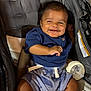 Frankie is registered to the contest to win money with this photo: baby, child, smiling, stroller, bottle, blue_shirt, shorts, infant, happy, portrait, person, seatbelt, fabric, comfort, cute, young, sitting, indoors, cheerful, casual