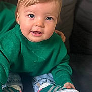 Imran participe au concours pour gagner de l'argent avec cette photo : toddler, child, green_sweater, blue_eyes, sneakers, jeans, couch, indoor, casual_clothing, portrait, cute, smiling, sitting, young_child, person, comfortable, fashion, footwear, happy, closeup