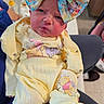 baby, infant, child, portrait, face, eyes, serious_expression, yellow_outfit, hat, cartoon_print, winnie_the_pooh, clothing, sitting, indoor, chair, caregiver, bottle, blanket, close_up, photography
