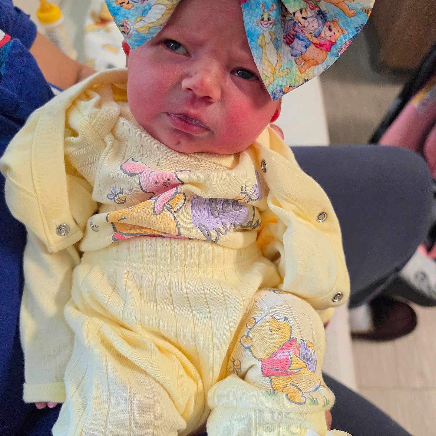 Adeline joined the competition — help win amazing prizes! baby, infant, child, portrait, face, eyes, serious_expression, yellow_outfit, hat, cartoon_print, winnie_the_pooh, clothing, sitting, indoor, chair, caregiver, bottle, blanket, close_up, photography