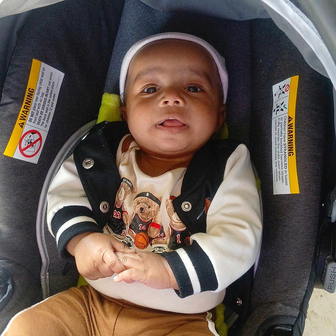 Genesis is registered to the contest to win money with this photo: baby, infant, child, car_seat, sitting, portrait, face, eyes, tongue, smiling, curious, clothing, jacket, pants, bear_design, headband, hands, indoor, photography,  안전