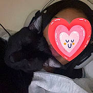 Sonic participe au concours pour gagner de l'argent avec cette photo : cat, black_cat, person, headphones, heart_sticker, face_cover, text_overlay, french_text, indoor, bedroom, bed, blanket, cozy, cuddling, pet, portrait, selfie, dark_fur, casual, gaming