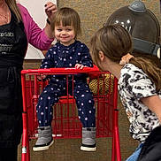 Lana joined the competition — help win amazing prizes! toddler, child, shopping_cart, pajamas, boots, woman, apron, hairdryer, indoor, playful, smile, person, red, interaction, background, textured_wall, ponytail, clothing, furniture, candid