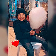 Gabriel a rejoint le concours — aidez-le/la à gagner de superbes lots ! child, kid, smiling, cotton_candy, beanie, jacket, jeans, stool, indoor, festive_lights, holiday_decor, portrait, snack, happy, chair, window, reflection, heart_sticker, tiled_floor, christmas_tree