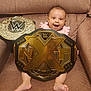 Na'Hijah is registered to the contest to win money with this photo: baby, smiling, wwe_championship_belt, champion, couch, brown_couch, happy, infant, person, barefoot, wrestling, belt, gold, sitting, indoors, cute, young_child, celebration, victory, portrait
