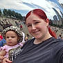 woman, baby, selfie, red_hair, leopard_print, hat, pink_clothing, cloud_gate, millennium_park, chicago, reflection, crowd, urban, skyscraper, outdoor, daytime, smile, tourist, cityscape, public_space