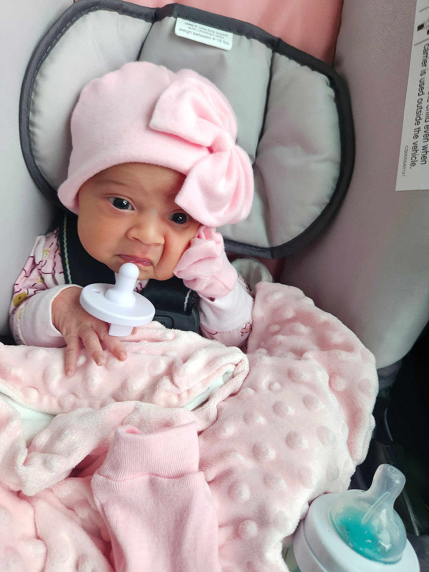 Na'Hijah is registered to the contest to win money with this photo: baby, infant, pink_hat, pacifier, blanket, car_seat, baby_bottle, clothing, face, hand, cute, newborn, soft_texture, indoors, person, child, warm, cozy, seatbelt, accessory