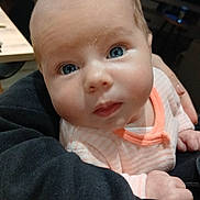 Mía participe au concours pour gagner de l'argent avec cette photo : arm, baby, blue_eyes, child, close_up, clothing, cozy, curious, expression, face, furniture, hand, indoor, infant, peach_stripes, person, portrait, skin, television, wooden_beams