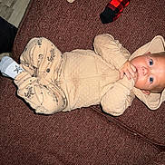 Kane is registered to the contest to win money with this photo: baby, child, onesie, hood, bear_ears, blue_eyes, couch, brown_couch, socks, hand, fingers, cute, infant, indoor, fabric, clothing, portrait, lying_down, looking_at_camera, cozy