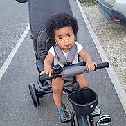 Lorenzo participe au concours pour gagner de l'argent avec cette photo : baby, car, child, curious, curly_hair, face, greenery, handlebars, outdoor, pavement, person, road, sandals, seatbelt, sidewalk, stroller, toddler, transportation, tricycle, vehicle