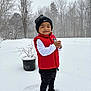 child, toddler, snow, winter, beanie, hat, red_vest, white_long_sleeve, black_pants, boots, smile, outdoors, trees, potted_plant, snowflakes, standing, portrait, playful, backyard, cold_weather