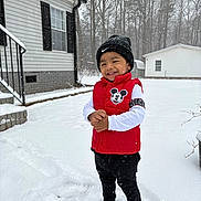 Arturo is registered to the contest to win money with this photo: child, toddler, smile, snow, winter, beanie, red_vest, mickey_mouse, house, backyard, trees, snowflakes, boots, jacket, outdoor, smiling, happy, standing, cold, footprints