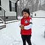 child, toddler, smile, snow, winter, beanie, red_vest, mickey_mouse, house, backyard, trees, snowflakes, boots, jacket, outdoor, smiling, happy, standing, cold, footprints