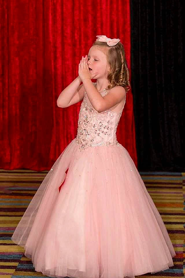 Hannah is registered to the contest to win money with this photo: arm, bridal_clothing, bridal_party_dress, curtain, day_dress, dress, face, facial_expression, fashion_design, flash_photography, gown, hair, happy, magenta, one_piece_garment, person, pink, shoulder, toddler, wedding_ceremony_supply