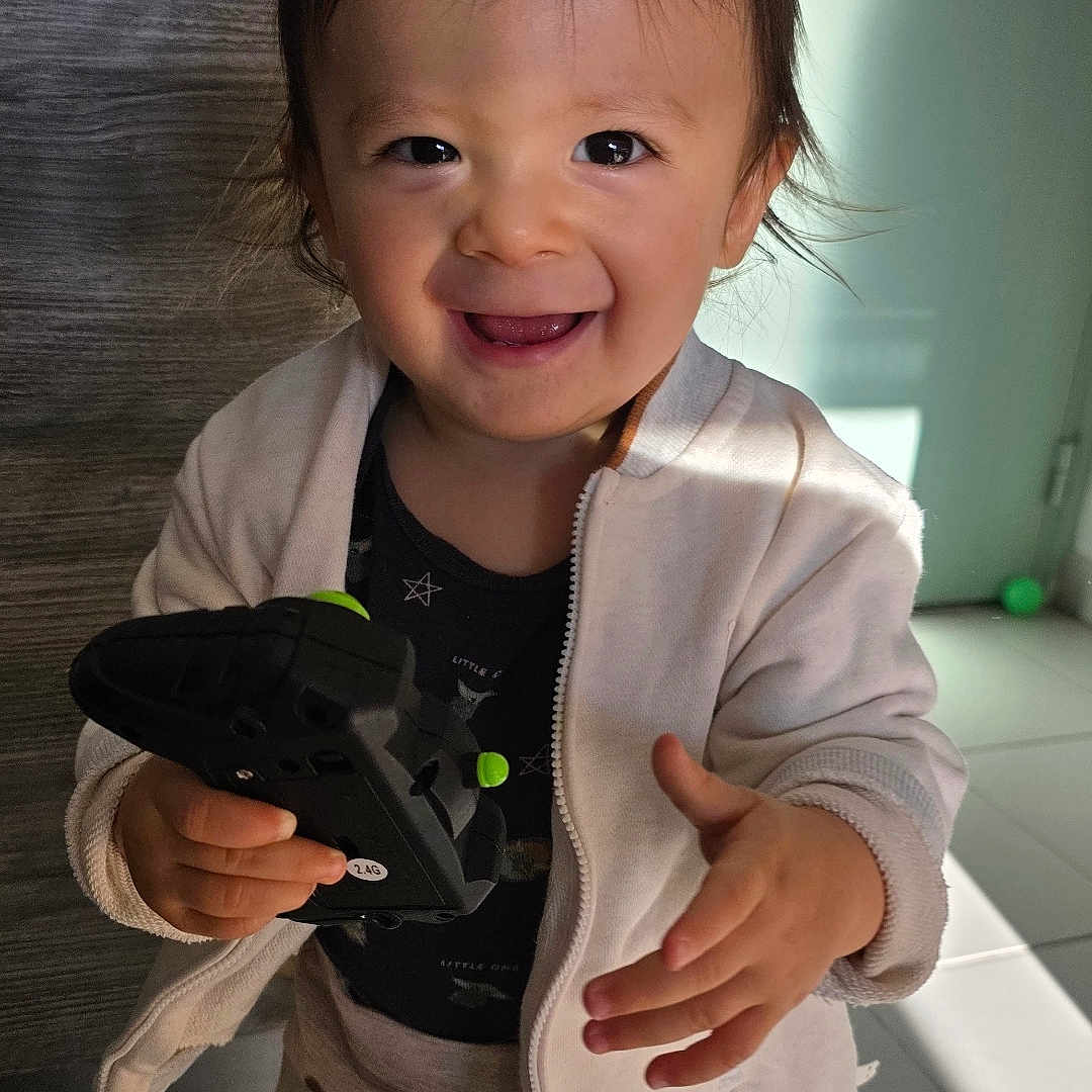 Lenny participe au concours pour gagner de l'argent avec cette photo : child, controller, cute, door, face, floor, green_toy, hand, happy, indoor, jacket, light, pants, person, play, shadow, smiling, standing, toddler, toy