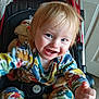toddler, child, smiling, stroller, colorful_clothing, animal_print, indoor, blanket, happy, cute, baby, seatbelt, face, blue_eyes, hand, portrait, playful, cheerful, young_child, hair