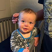 Dawson joined the competition — help win amazing prizes! baby, child, infant, crib, nursery, standing, smiling, happy, portrait, face, eyes, short_hair, camouflage_clothing, pajamas, adult, hand, bedroom, indoor, furniture, photography
