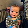 baby, child, infant, crib, nursery, standing, smiling, happy, portrait, face, eyes, short_hair, camouflage_clothing, pajamas, adult, hand, bedroom, indoor, furniture, photography