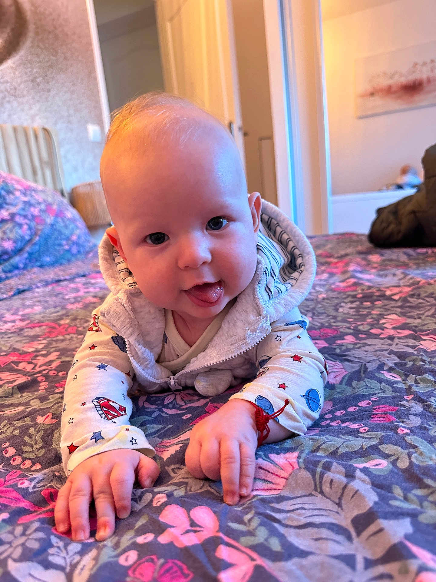 Christian participe au concours pour gagner de l'argent avec cette photo : baby, child, indoor, bed, blanket, floral_pattern, cute, tongue_out, face, hands, clothing, hoodie, playful, smiling, person, infant, room, soft_light, colorful, portrait