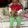 Tariyah is registered to the contest to win money with this photo: toddler, child, kitchen, counter, snack, cheetos, red_shirt, green_leggings, boots, toy_laptop, smile, hair_bows, sitting, indoor, cup, cabinet, happy, playing, beads, person