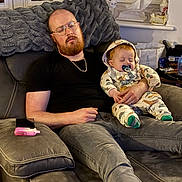 Stanley joined the competition — help win amazing prizes! man, baby, sleeping, couch, living_room, glasses, beard, pacifier, hoodie, blanket, window, tissue_box, remote_control, phone, casual_clothing, home_interior, relaxation, seated, indoor, family