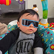Caleb joined the competition — help win amazing prizes! baby, infant, sunglasses, baby_seat, play_gym, toy, colorful, striped_clothing, hand, face, hair, indoor, floor, plush_toy, patterned_fabric, candid, portrait, cool, sitting, seat_cushion