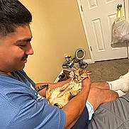 Coco is registered to the contest to win money with this photo: man, cat, bed, indoor, blue_shirt, short_hair, carpet, door, plastic_bag, socks, holding, pet, feline, casual, relaxed, home, person, animal, brown_cat, male