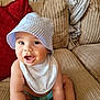 Elijah joined the competition — help win amazing prizes! baby, bucket_hat, bib, couch, plush_toy, books, infant, smiling, cute, indoor, child, face, sitting, clothing, homedecor, toy, expression, person, comfortable, curious