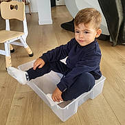 Noam a rejoint le concours — aidez-le/la à gagner de superbes lots ! toddler, child, plastic_bin, socks, navy_blue_clothing, wooden_floor, indoor, furniture, chair, home, playful, sitting, person, floor, light, casual_clothing, cute, young_child, smiling, relaxed