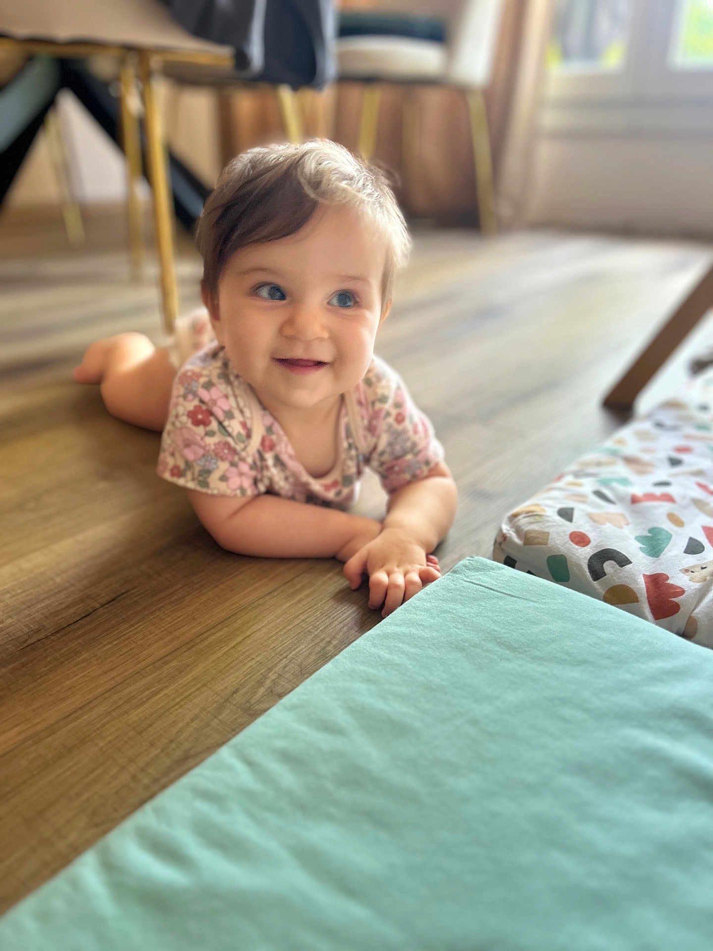 Louise a rejoint le concours — aidez-le/la à gagner de superbes lots ! baby, child, infant, floor, wooden_floor, onesie, floral_pattern, play_mat, indoors, natural_light, smiling, happy, cute, person, young_child, toddler, bright_eyes, crawling, home, soft_lighting