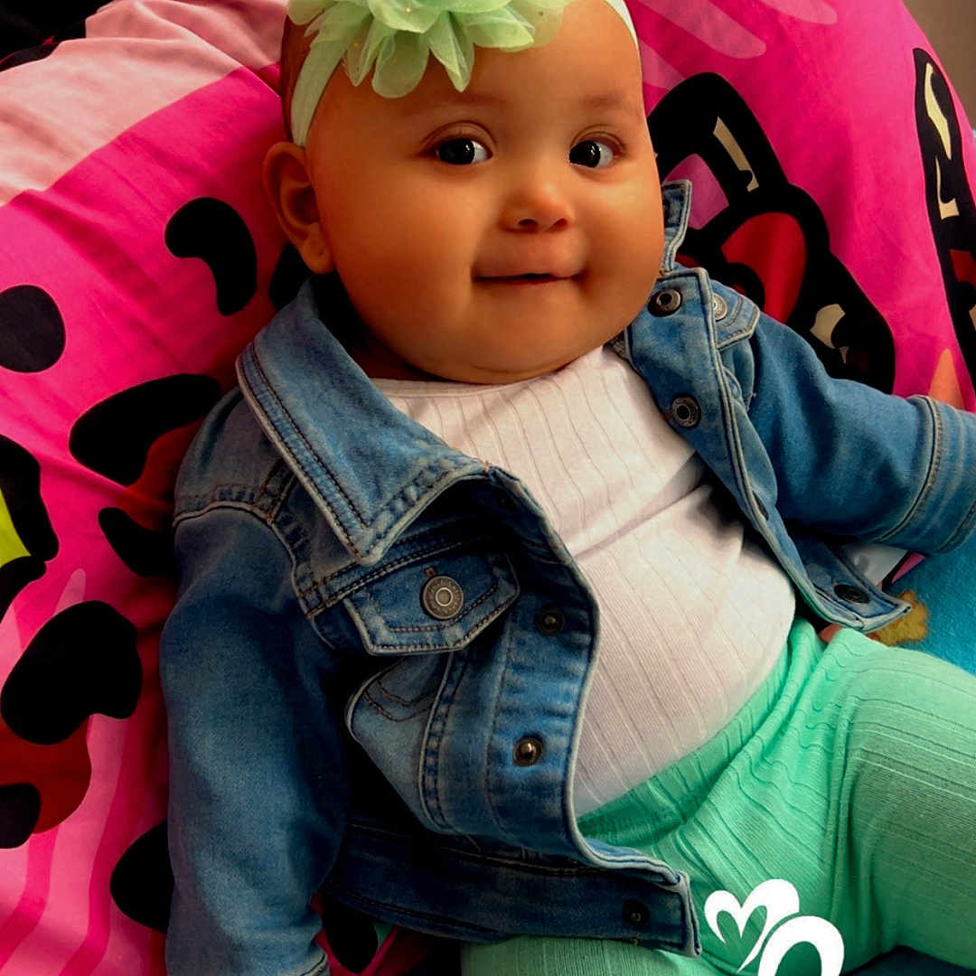 Kaylanee joined the competition — help win amazing prizes! baby, child, clothing, colorful_blanket, cozy, cute, denim_jacket, face, flower, furniture, happy, headband, indoors, person, pink_blanket, playful, portrait, sitting, smile, toddler