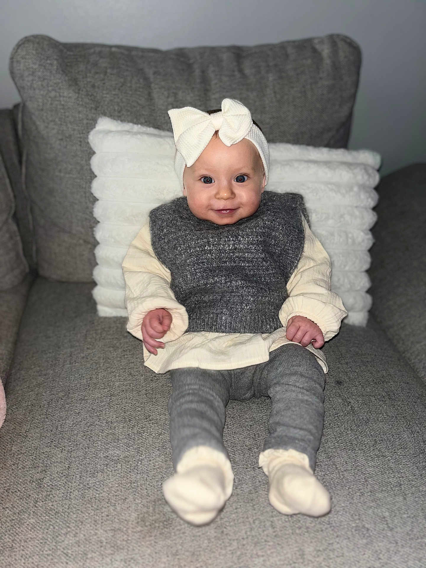 Eliana a rejoint le concours — aidez-le/la à gagner de superbes lots ! baby, child, smiling, headband, bow, couch, pillow, grey, knitwear, sitting, clothing, socks, indoor, portrait, cute, happy, infant, cozy, soft, face