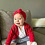 baby, child, red_headband, red_cardigan, white_sock, denim_skirt, couch, gray_couch, smiling, sitting, indoor, cute, portrait, happy, toddler, clothing, face, person, cozy, soft_lighting