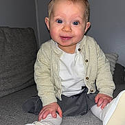 Eliana participe au concours pour gagner de l'argent avec cette photo : baby, child, smiling, blue_eyes, cardigan, white_shirt, gray_skirt, white_shoes, sitting, couch, indoor, person, happy, cute, infant, toddler, clothing, furniture, skin, hand