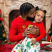 A'Keloni Dior Davis is registered to the contest to win money with this photo: child, adult_male, father, toddler, christmas, holiday_pajamas, matching_outfits, red_clothing, fireplace_backdrop, christmas_tree, holiday_decor, kiss, hug, braided_hair, pigtails, beard, plaid_blanket, living_room, portrait, festive