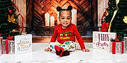 A'Keloni Dior Davis joined the competition — help win amazing prizes! candles, child, christmas, decorations, festive, fireplace, gifts, holiday, ornaments, patterned_pants, poinsettia, portrait, presents, red_shirt, sitting, smile, socks, studio_backdrop, toddler, tree
