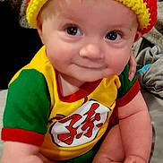 Victor joined the competition — help win amazing prizes! baby, infant, hat, knit_hat, pom_pom, colorful_clothing, yellow, red, green, smile, cute, sitting, bed, tattoo, arm, hand, foot, indoors, person, portrait